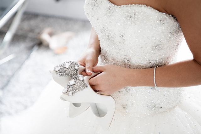 Žena v svadobných šatách rukách drží biele topánky 